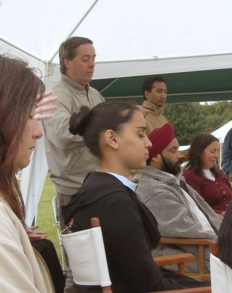 four seated people meditate with closed eyes in a gazebo, two instructors stand behind